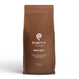 A brown bag displays Purity Coffee's "Protect," a medium roast organic whole bean coffee crafted for liver vitality.
