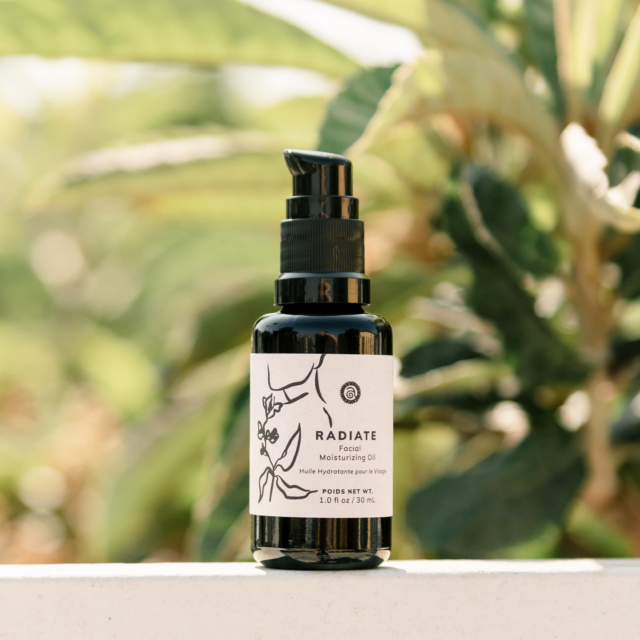 Radiate Facial Moisturizing Oil sits on a ledge against a blurred leafy background, showcasing its natural beauty product label.
