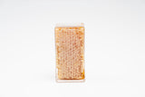 Beeswax honeycomb sits encased in a clear plastic container, showcasing natural honey.
