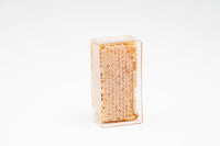 Honeycomb sits in a clear, rectangular container against a white backdrop, showcasing its natural golden honeycombs.
