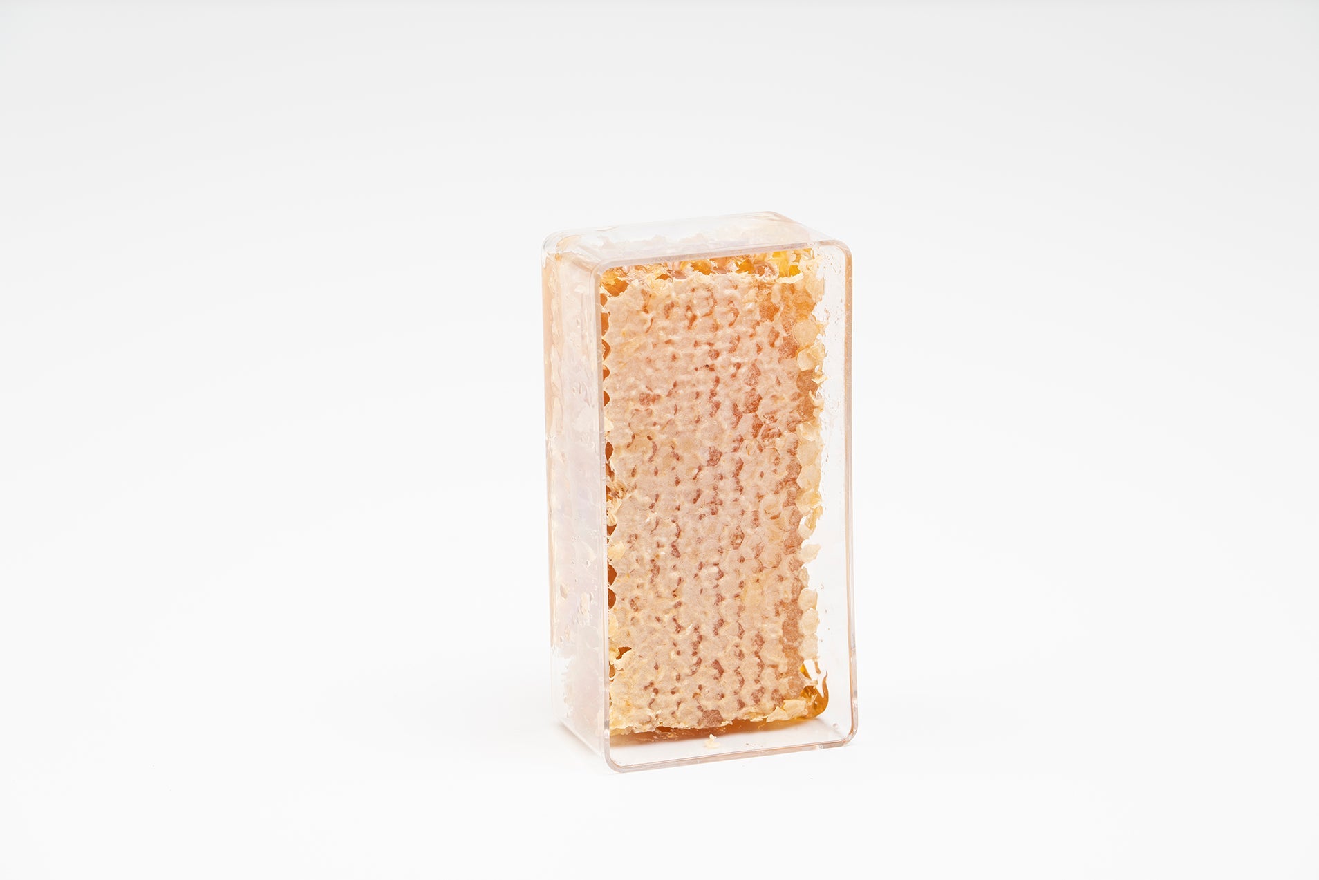 Honeycomb sits in a clear, rectangular container against a white backdrop, showcasing its natural golden honeycombs.
