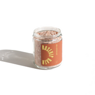 URB Apothecary's Rosehip Bath Soak sits in a clear jar with an orange label, casting a shadow on a white background.
