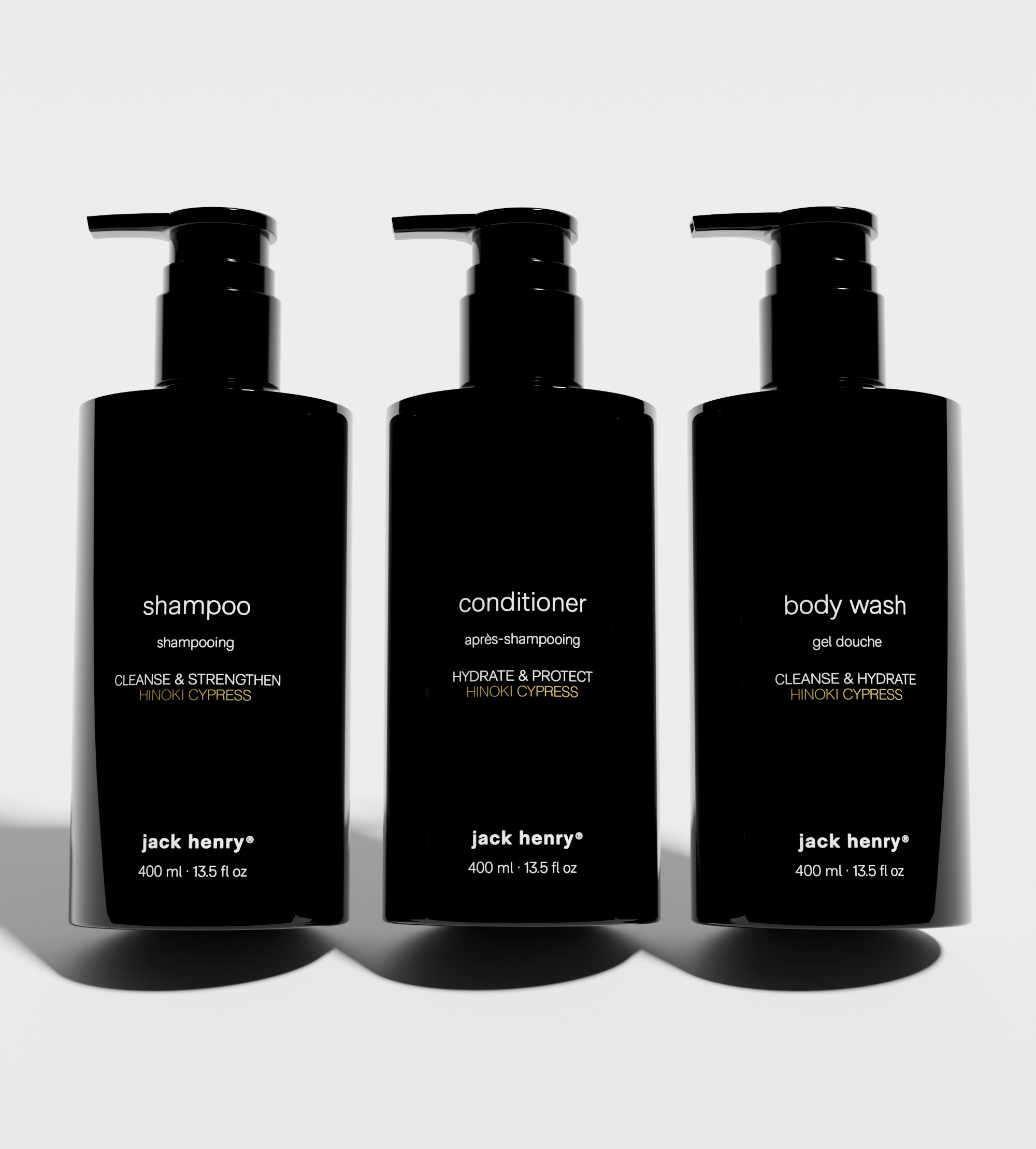 Three black pump bottles showcase Jack Henry shampoo, conditioner, and body wash with Hinoki Cypress scent.

