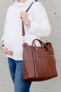 Pregnant woman carries a stylish brown leather diaper bag over her shoulder.
