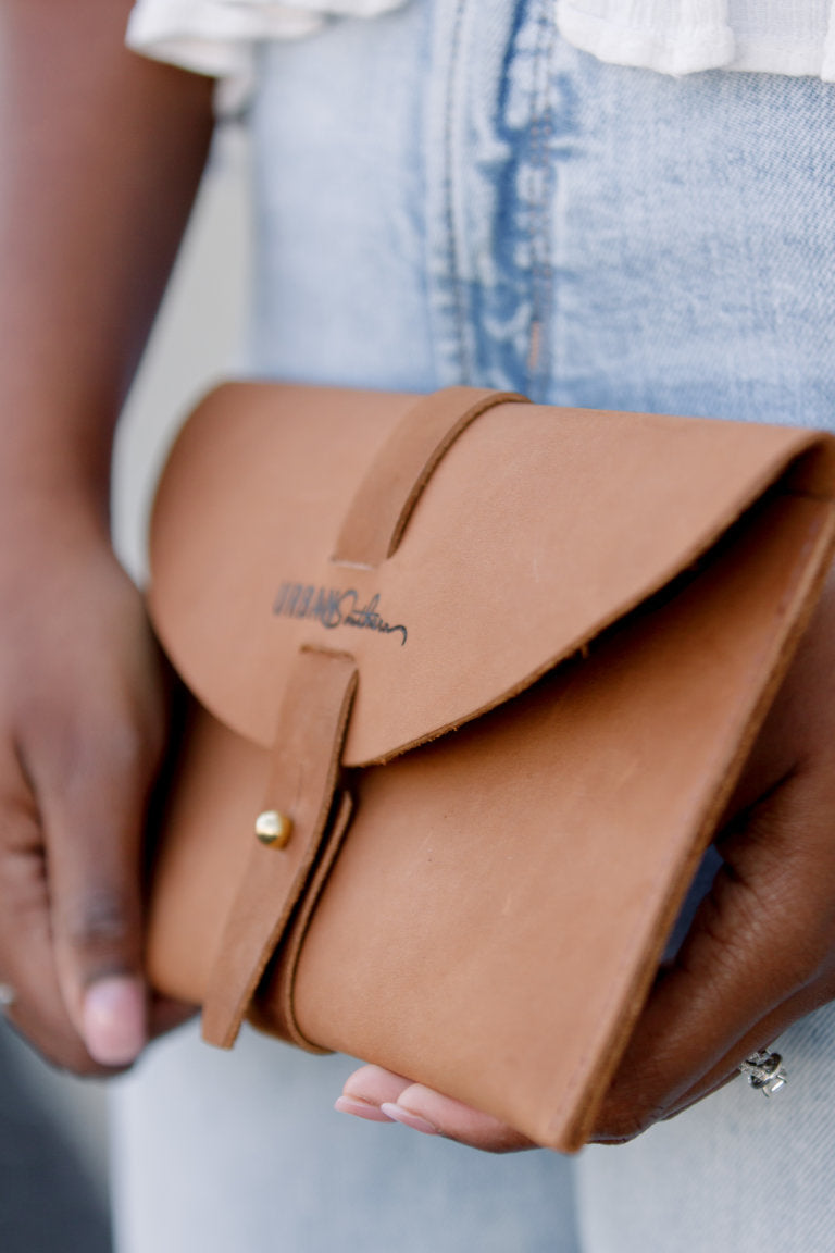 Woman in denim holds a stylish Urban Southern brown leather clutch with gold button closure.
