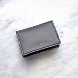 A black leather cardholder rests on a white marble surface.

