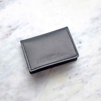 A black leather cardholder rests on a white marble surface.
