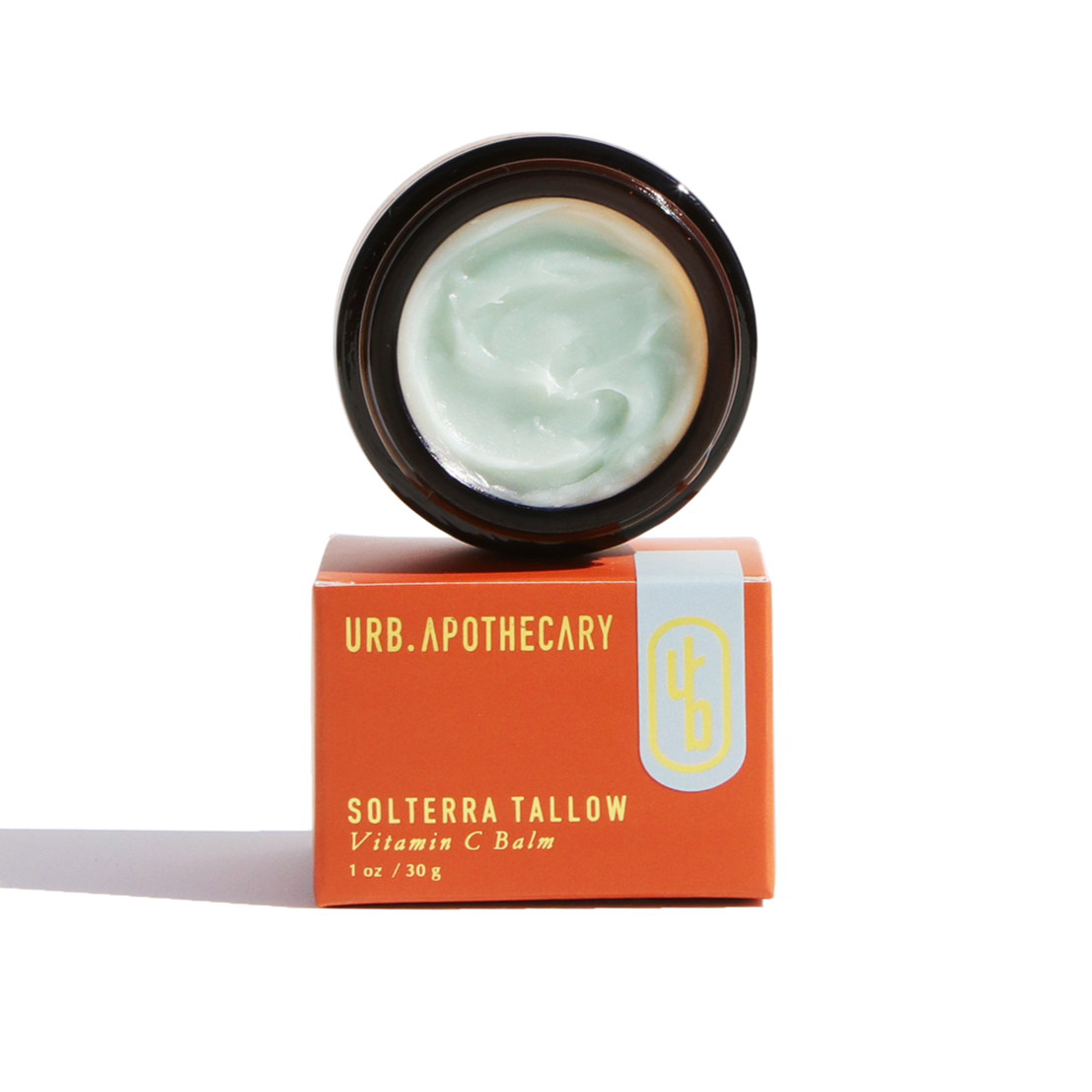 URB Apothecary Solterra Tallow Vitamin C Balm sits on its orange box, showcasing a light green cream inside.
