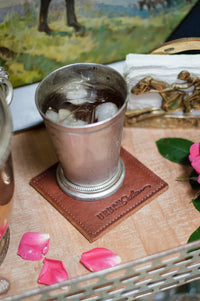 Iced tea chills in a silver julep cup on a leather coaster, part of a styled, equestrian-themed Southern hospitality display.
