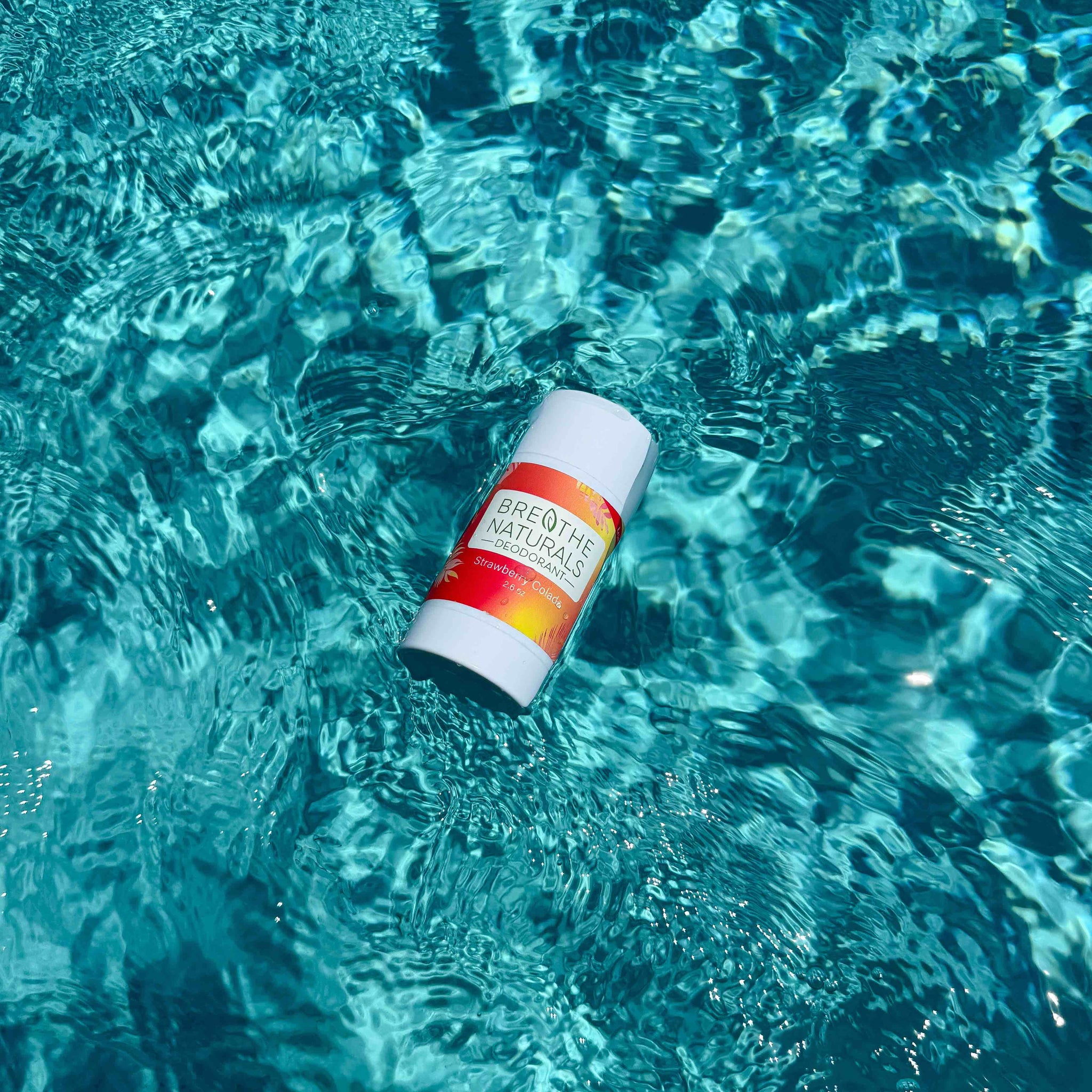 Breathe Naturals deodorant floats in shimmering turquoise pool water.
