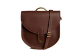 A stylish brown leather saddle bag with gold hardware sits against a white backdrop.
