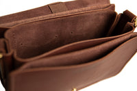 Open brown leather satchel reveals soft suede interior and multiple compartments.
