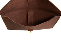An open brown leather clutch bag reveals its suede-lined interior and brass closure.
