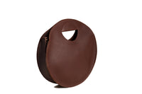 A brown leather circle bag with a handle sits on a white background.
