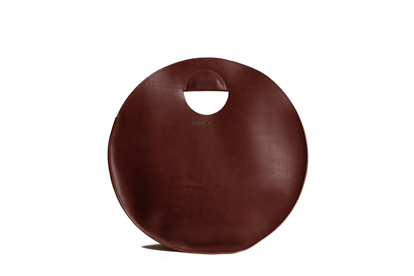 A stylish, round brown leather tote bag with a unique handle design sits against a white background.
