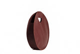 A stylish brown leather tote bag with a unique circular design stands upright against a white background.
