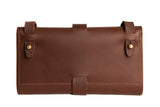 Displaying a closed brown leather wallet with brass button closures and a wraparound strap.
