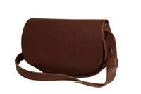 A brown leather satchel handbag with an adjustable shoulder strap sits on a white background.
