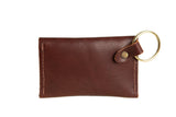 A brown leather cardholder with a gold keyring lays isolated on a white background.
