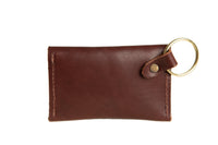 A brown leather cardholder with a gold keyring lays isolated on a white background.

