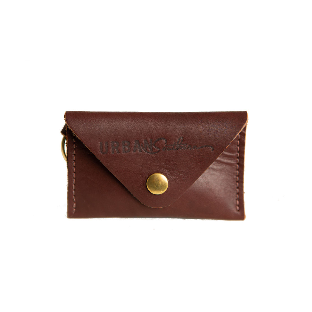 A dark brown leather card holder wallet featuring a brass snap closure and the "Urban Southern" logo is displayed against a white background.
