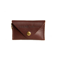 A dark brown leather card holder wallet featuring a brass snap closure and the "Urban Southern" logo is displayed against a white background.
