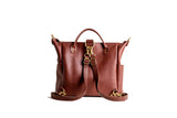 A stylish brown leather tote bag with gold hardware displays its convertible backpack straps on a white background.
