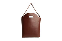 Displays a simple, stylish brown leather tote bag with a handle cutout and shoulder strap.
