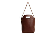 Display shows a stylish, minimalist dark brown leather tote bag with a unique cut-out handle and visible stitching.
