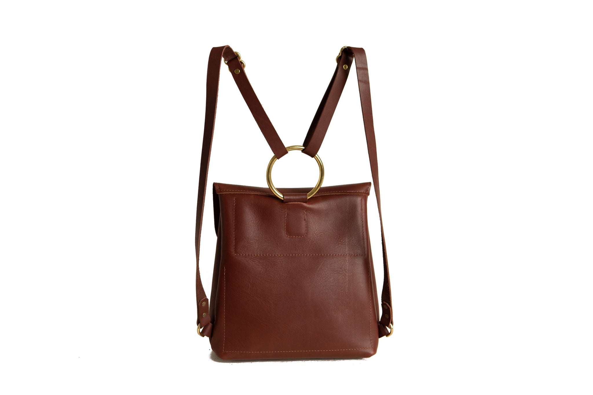 A brown leather backpack features a gold circular handle and adjustable straps, presented against a bright white background.
