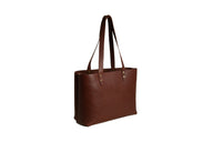 A handcrafted brown leather tote bag stands upright against a white backdrop.

