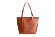 Showcases a handcrafted leather tote bag from Urban Southern, featuring rich brown tones and sturdy leather handles.
