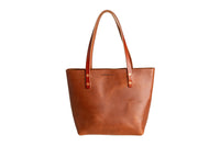 Showcases a handcrafted leather tote bag from Urban Southern, featuring rich brown tones and sturdy leather handles.
