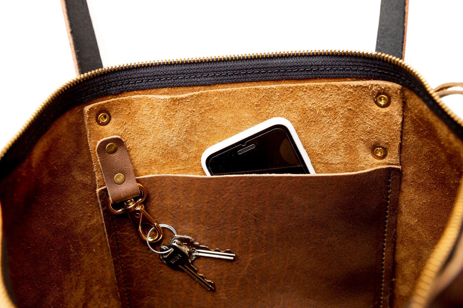 Inside a leather tote bag, a smartphone peeks from a pocket while keys hang from a brass clip.
