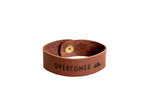 A brown leather bracelet displaying the word "OVERCOMER" and a mountain graphic rests on a white surface.
