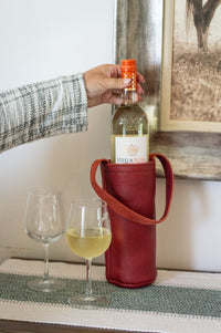 A woman prepares to pour a chilled bottle of Stella Rosa white wine into two wine glasses, presented in a stylish red leather wine tote.
