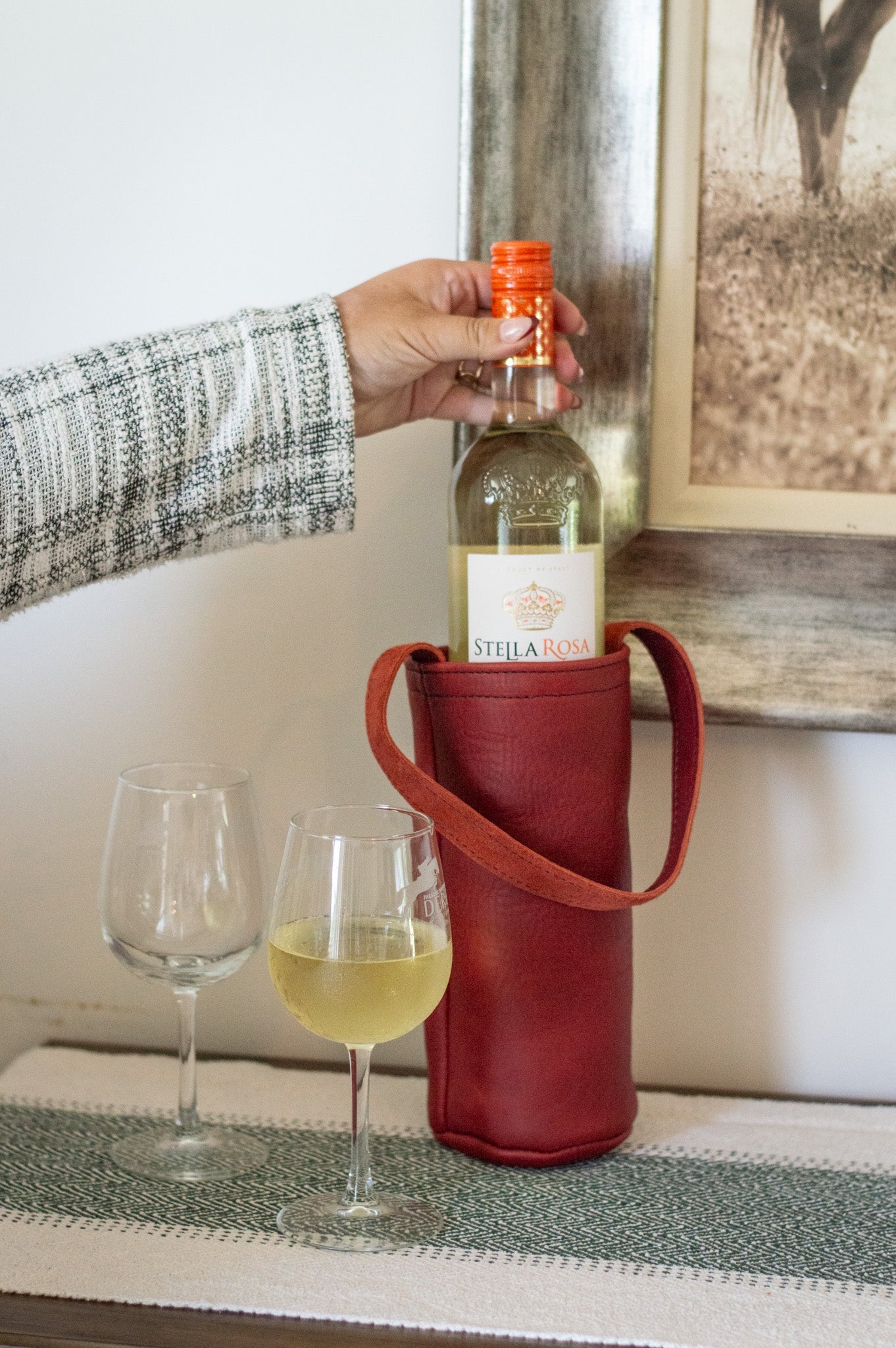A woman prepares to pour a chilled bottle of Stella Rosa white wine into two wine glasses, presented in a stylish red leather wine tote.
