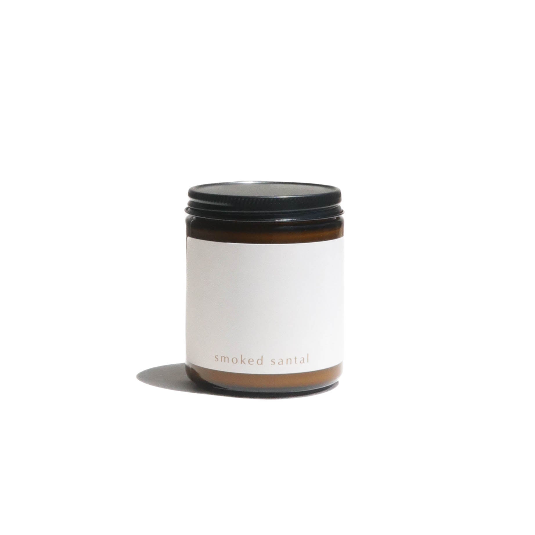A scented candle labeled "smoked santal" sits isolated on a white surface, casting a soft shadow.
